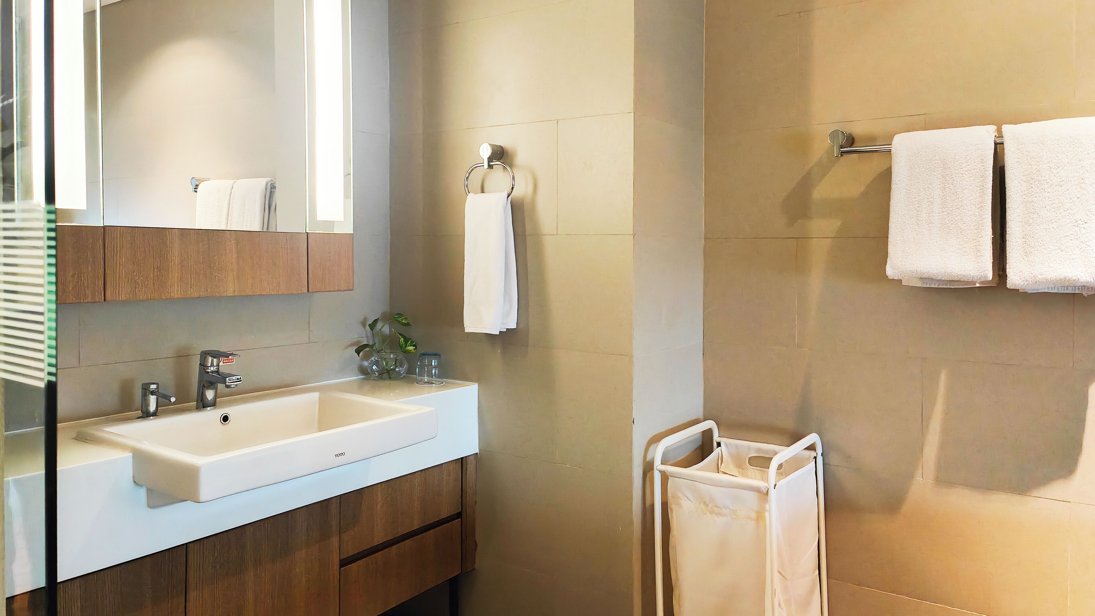 A modern bathroom with a white sink, wooden cabinets, a mirror, and two towels hanging on a towel rack.