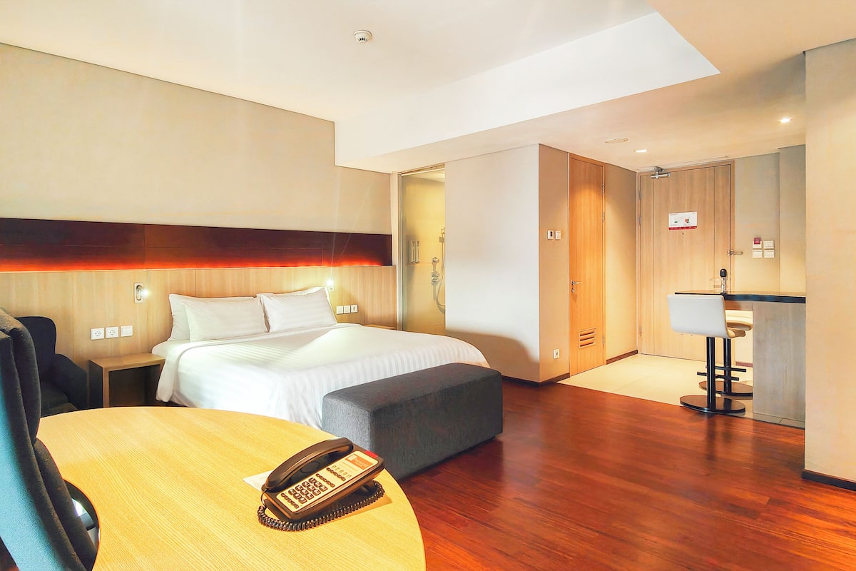 A hotel room with a bed, a desk with a telephone, a chair, a small table, and a mirror.