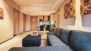 Una sala moderna con un sofá gris, un otoman negro y una zona de comedor con dos sillas negras.