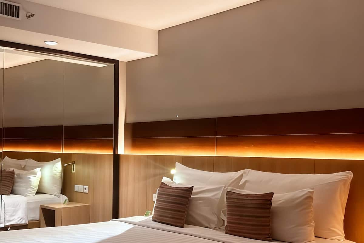 A modern hotel room with a large bed, a bedside table, a mirror, and a wall-mounted light fixture.
