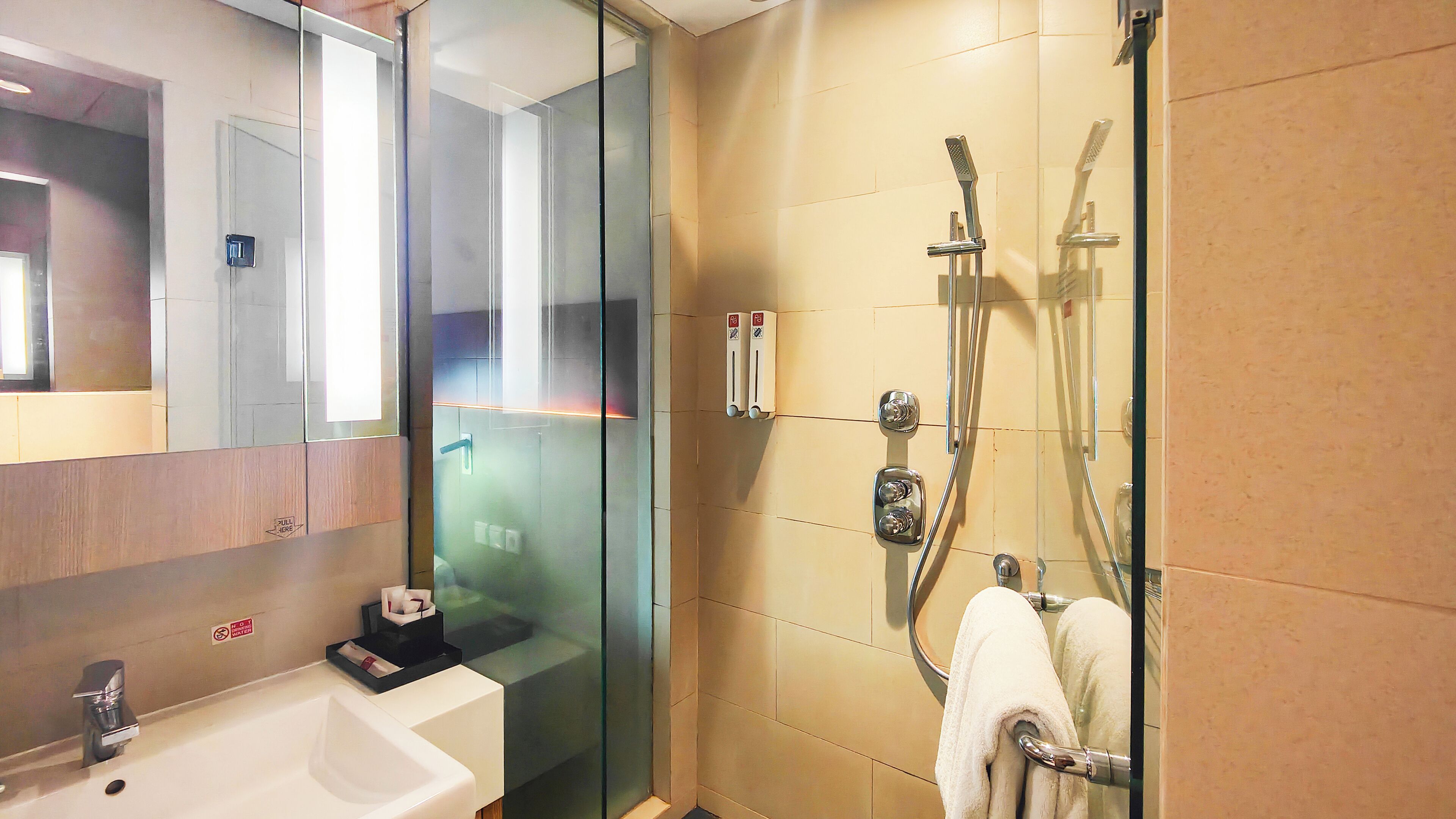 A modern bathroom with a glass shower enclosure, a sink with a soap dispenser, and a towel rack.