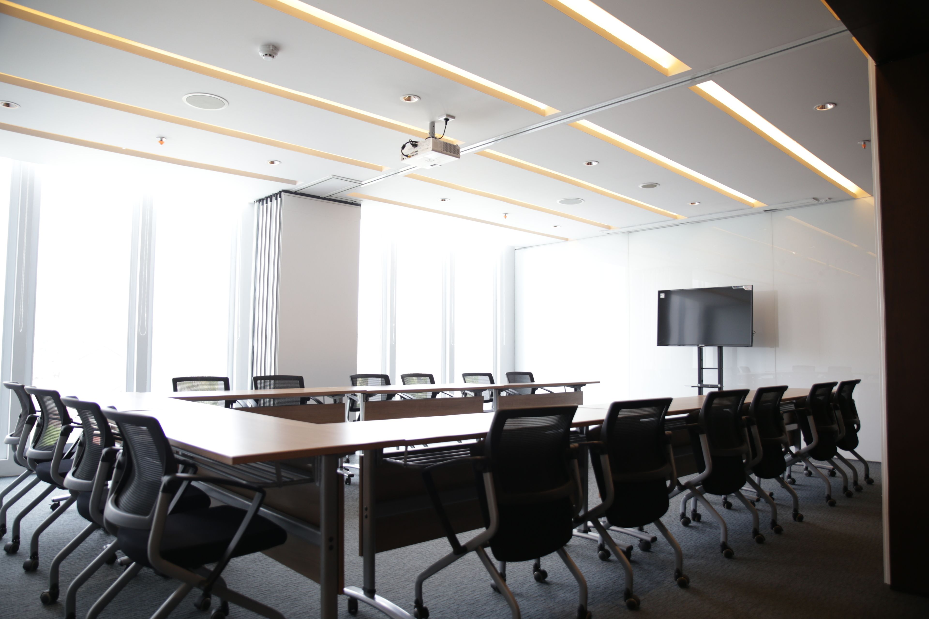A conference room with a long table, multiple chairs, a projector, and a TV screen.