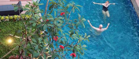 A swimming pool with a person in the water, surrounded by plants and a wooden deck.