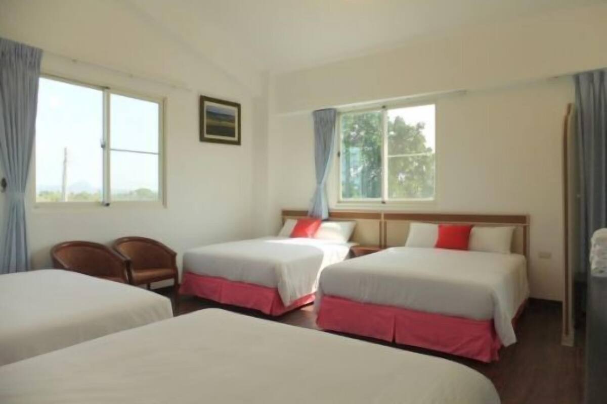 A hotel room with two beds, a chair, and a window with curtains.