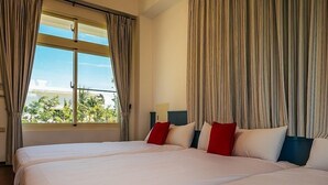Hotellihuone, jossa on kaksi sänkyä, suuret ikkunat ja verhot.