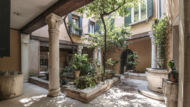 A courtyard with stone columns, potted plants, and a tiled floor.