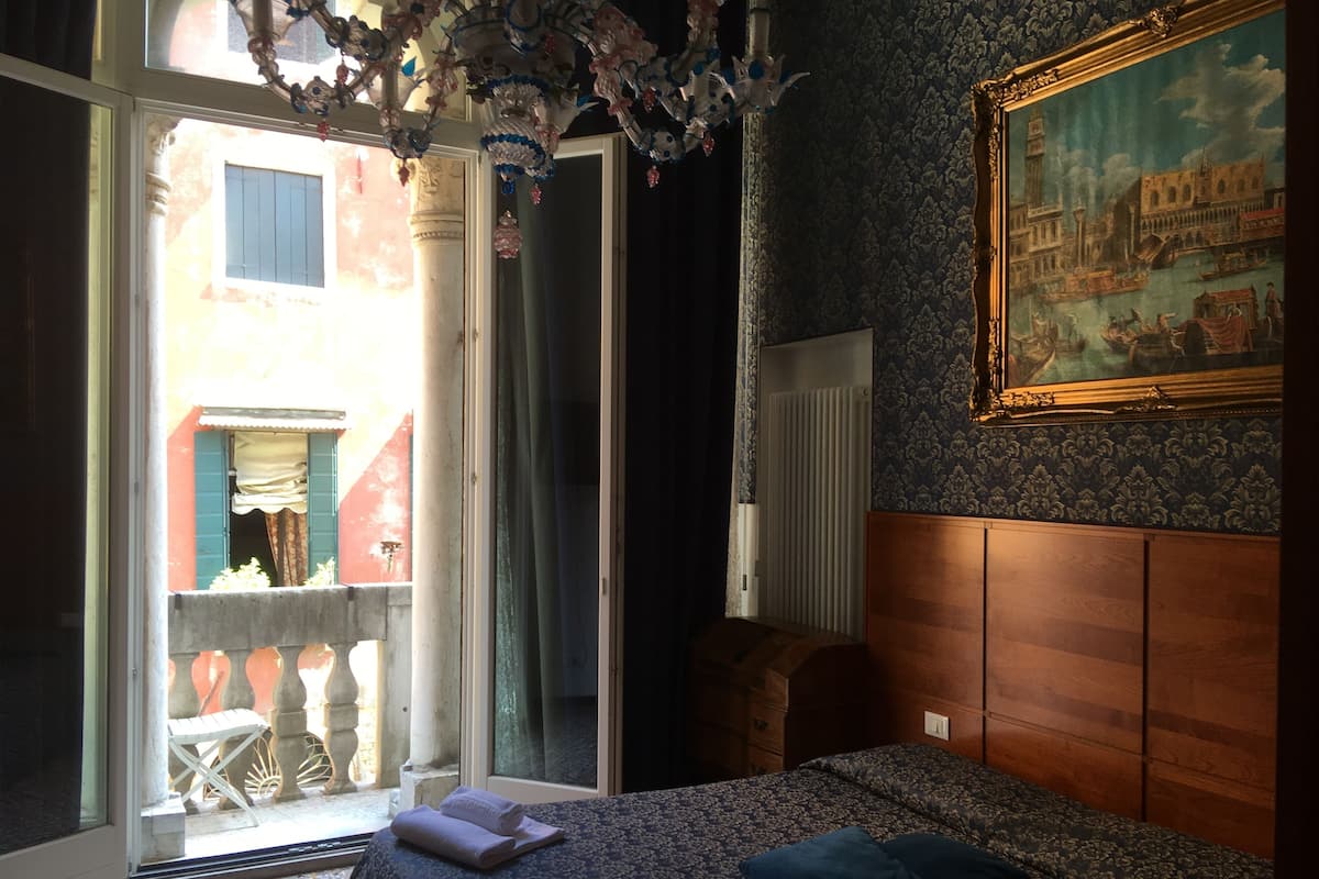 A bedroom with a bed, a painting, a window, and a view of a building outside.