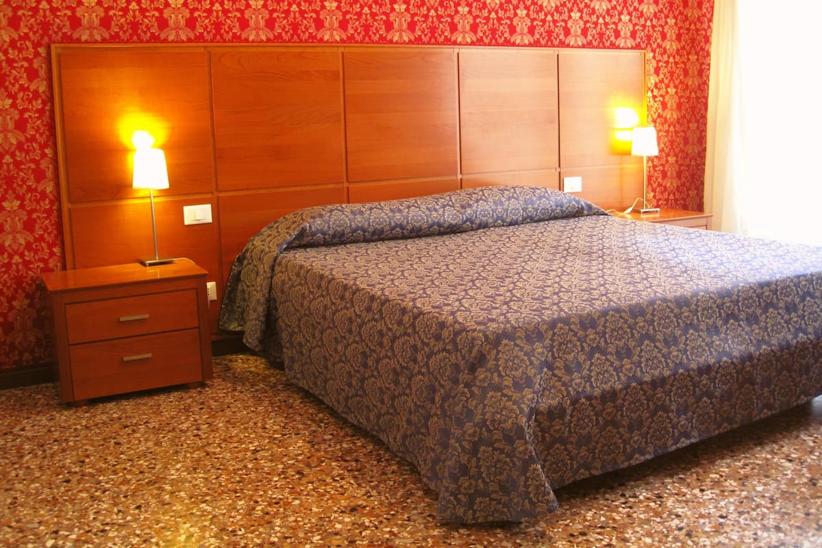 A hotel room with a large bed, two bedside tables with lamps, a wooden headboard, and a carpeted floor.