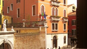 A canal with gondolas, a statue, and buildings with balconies and flags.