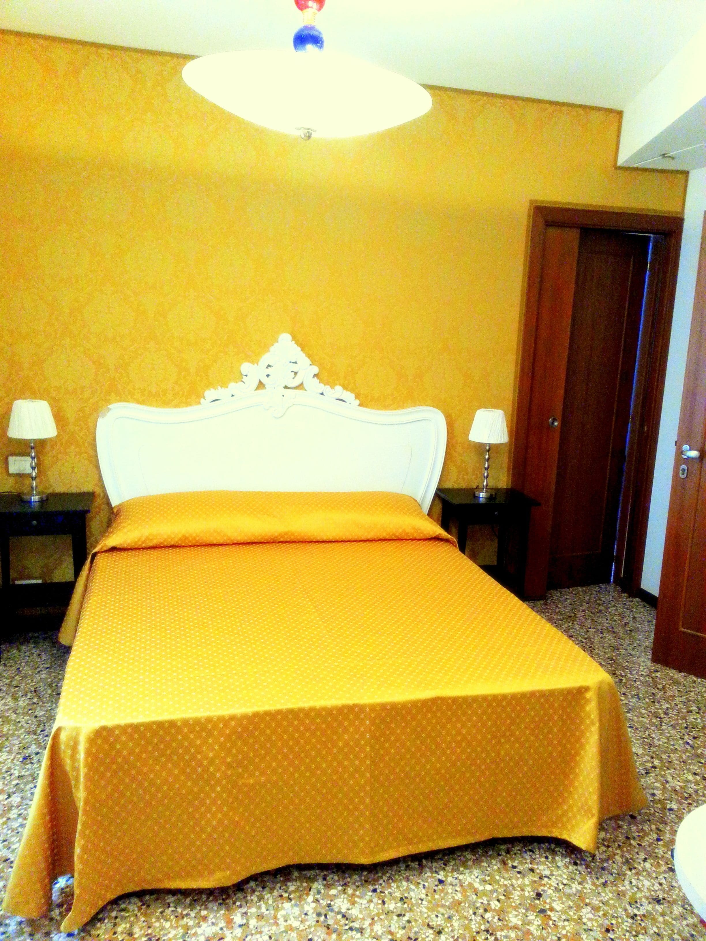 Habitación de hotel con una cama grande, dos mesitas de noche con lámparas, una puerta de madera y suelo alfombrado.