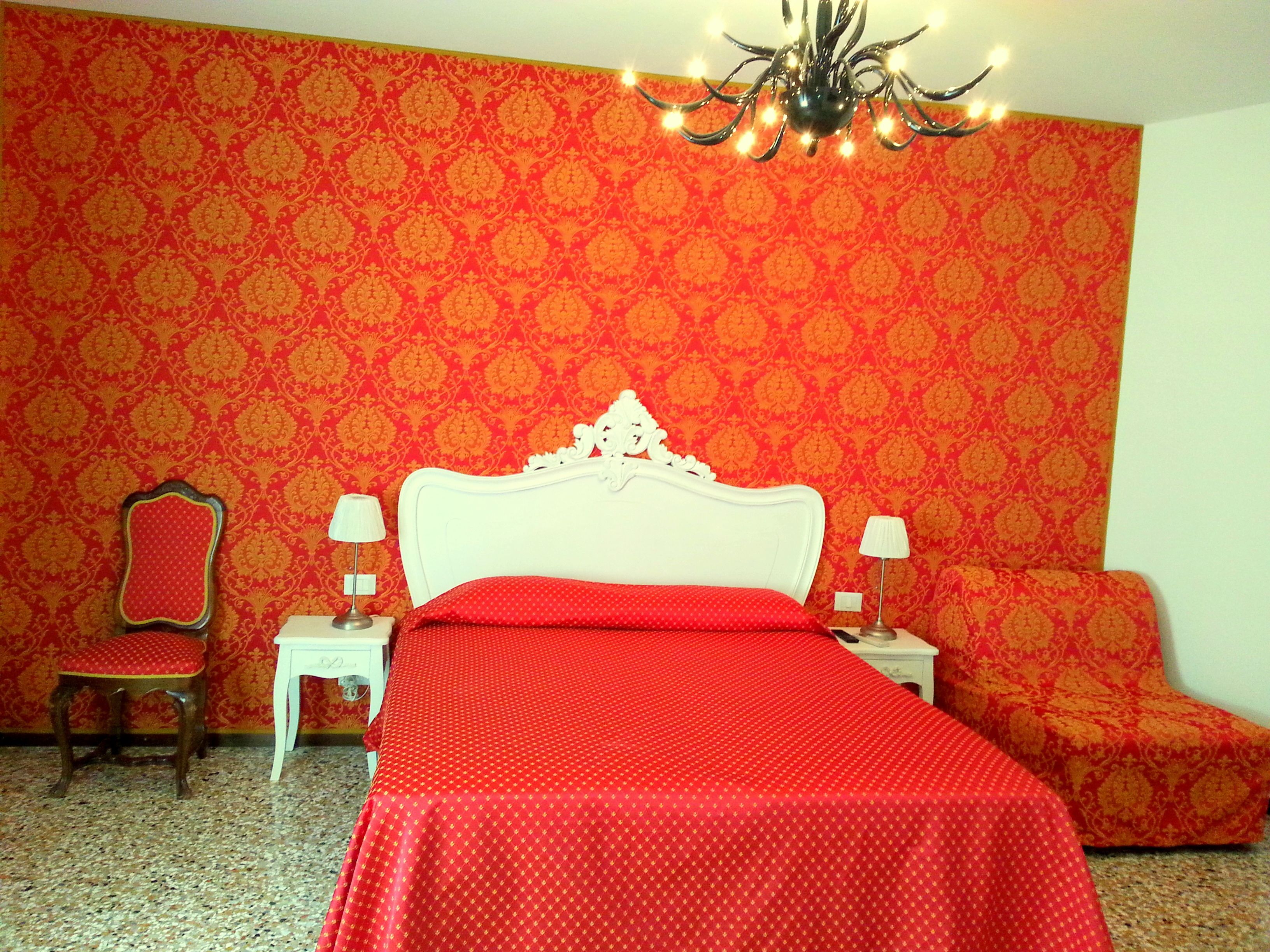 Una habitación con cama, dos mesitas de noche, una silla y una araña.