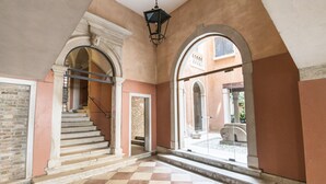 A hallway with a checkered floor, a staircase, and arched doorways leading to an outdoor area.