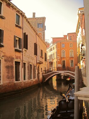 A narrow canal with buildings on either side, a bridge, and a gondola in the water.