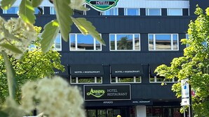 A hotel building with multiple signs indicating it is a hotel and restaurant. There are several cars parked in front, and the building has a modern architectural style with a dark facade and multiple windows. - Hotel Amado (Pori)