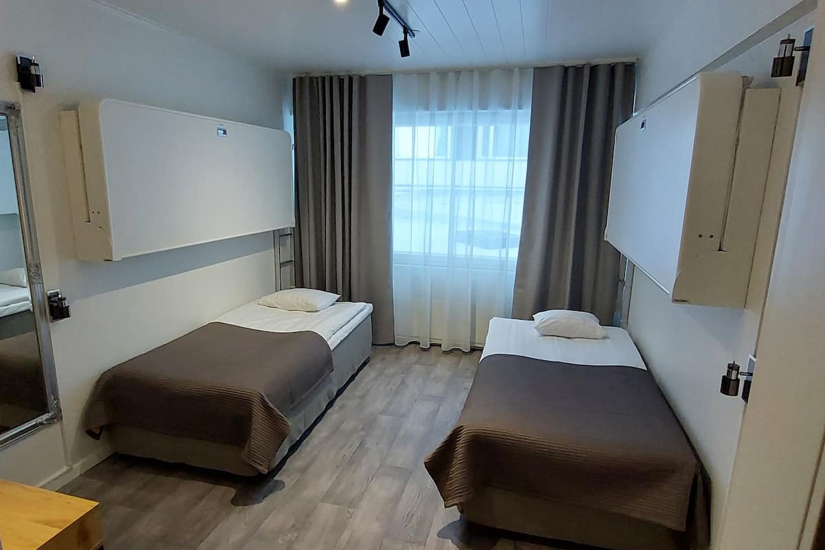 A hotel room with two single beds, a large mirror, a wardrobe, and a window with curtains.
