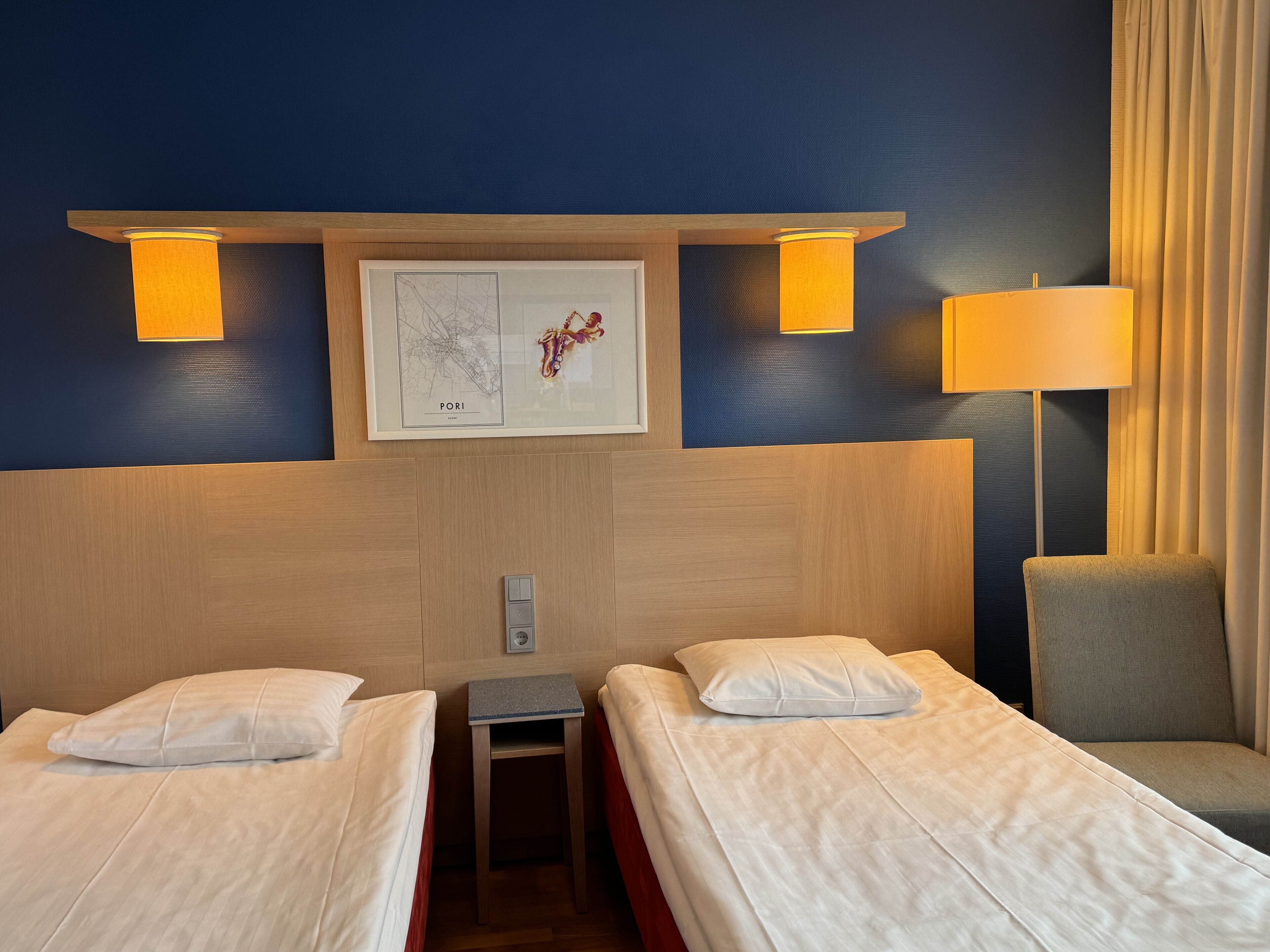 A hotel room with two beds, a small table, a chair, and a wall-mounted map.