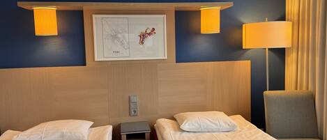 A hotel room with two beds, a small table, a chair, and a wall-mounted map.