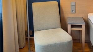 A hotel room with a grey upholstered armchair, a floor lamp, a small bedside table, and a headboard. - Hotel Amado (Pori)