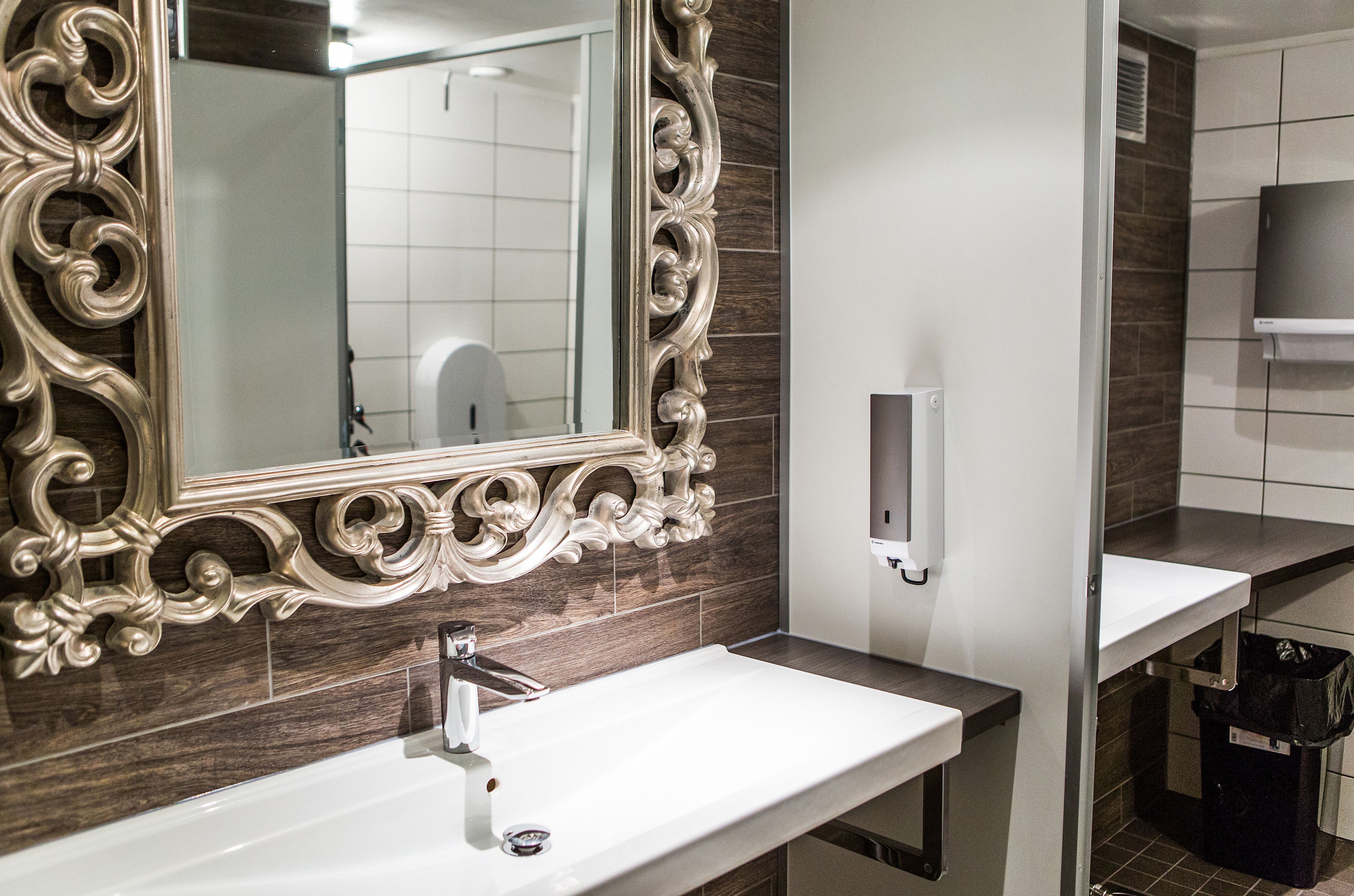 A bathroom with a large ornate mirror, a white sink, and a black trash bin.