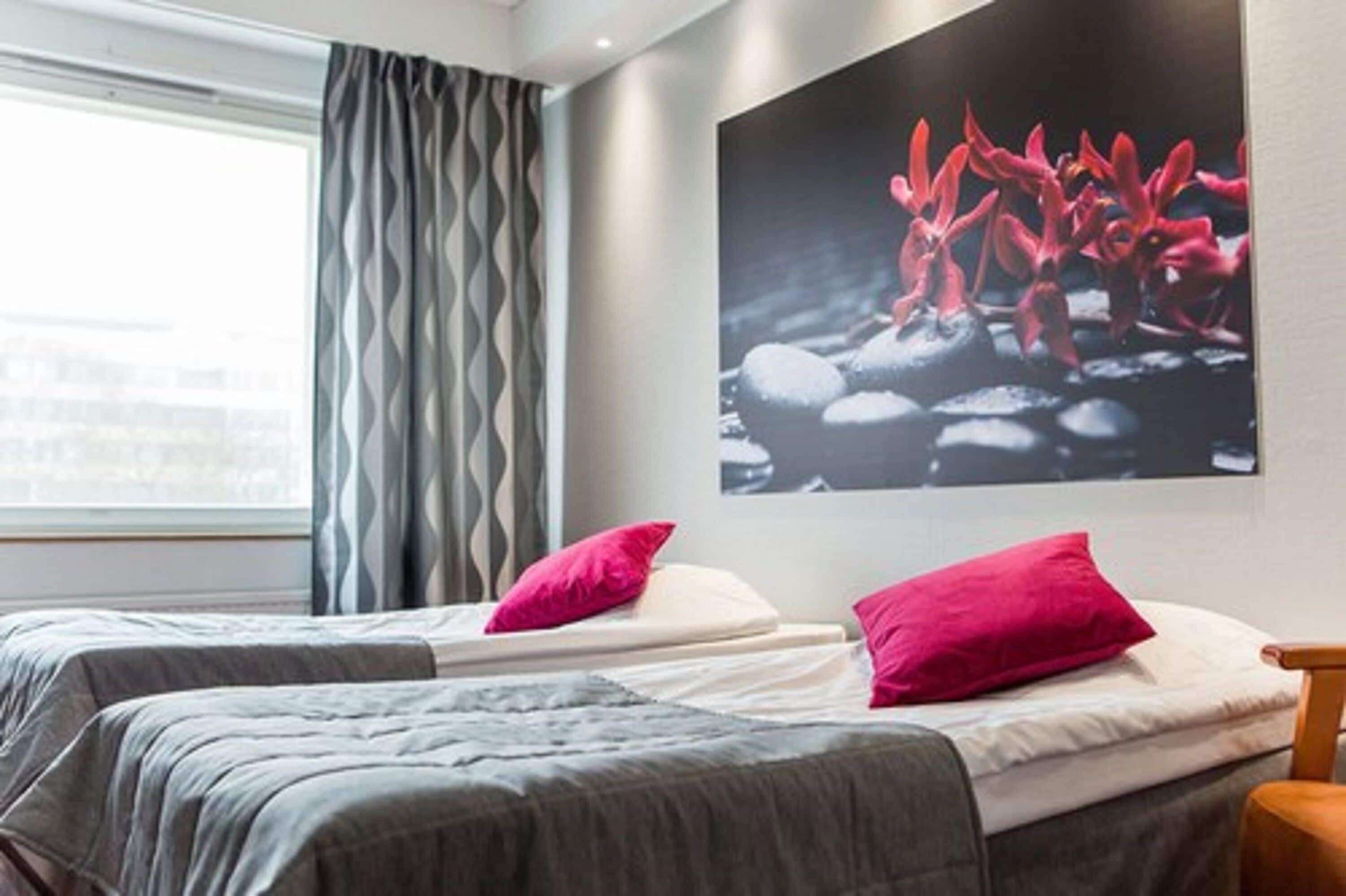 Una camera d'albergo con due letti, un'ampia finestra con tende e un'opera d'arte appesa al muro.