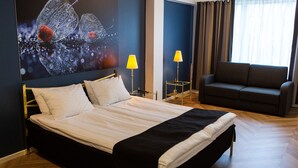 A hotel room with a large bed, two bedside lamps, a sofa, and a wall art piece. - Hotel Amado (Pori)