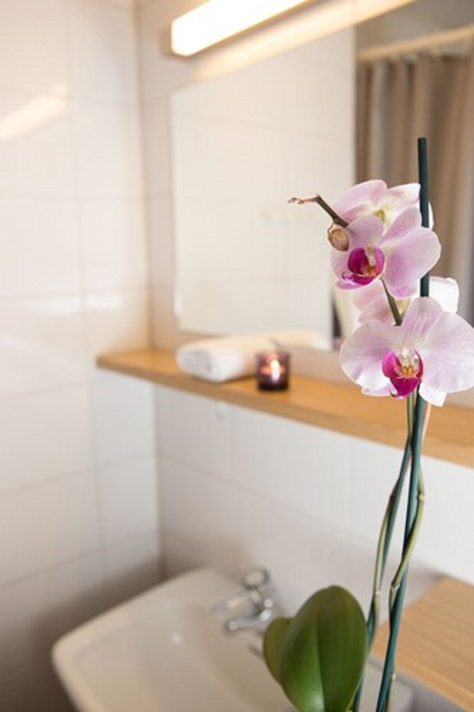Un baño con un lavamanos blanco, un espejo y un estante con una vela.