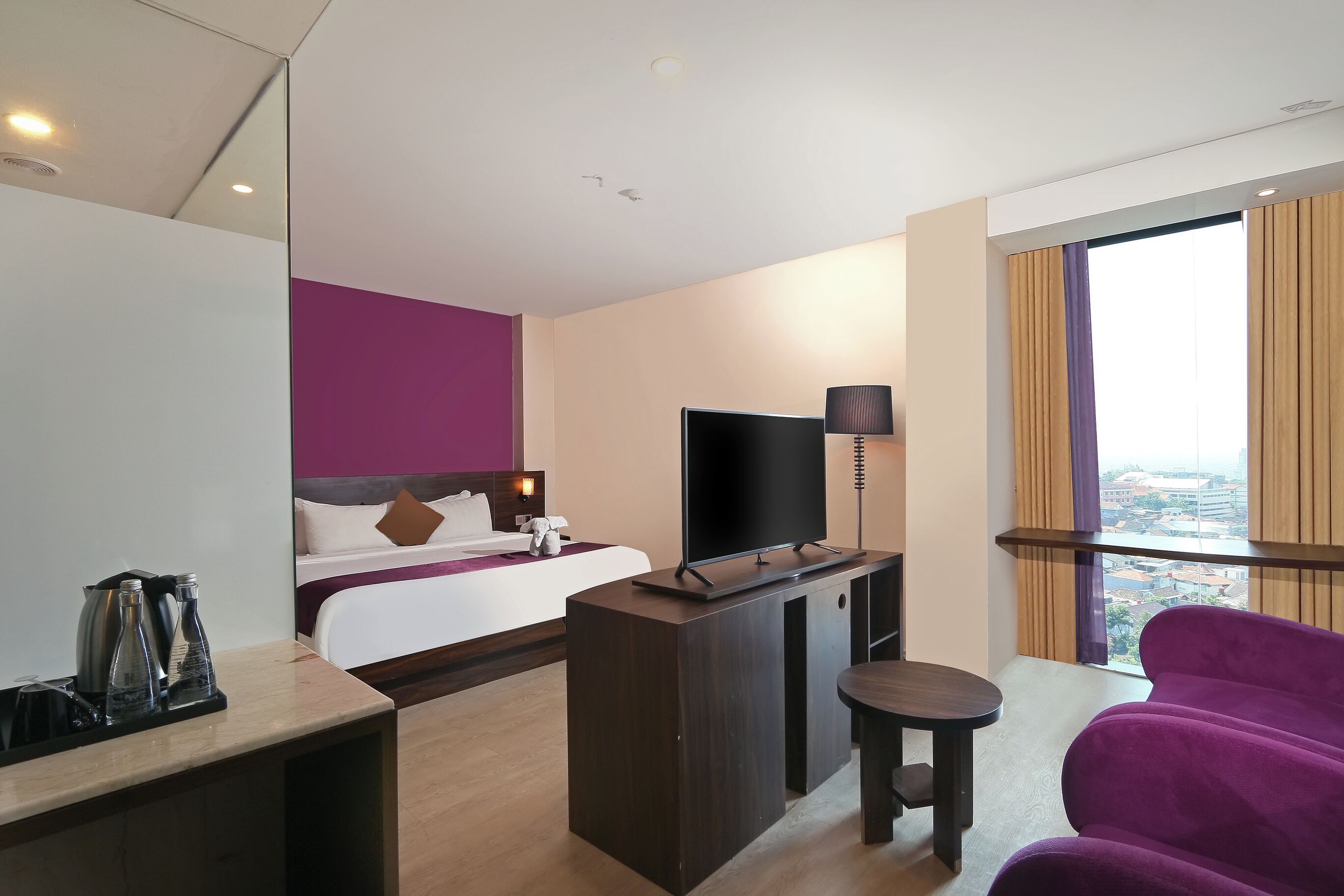 Habitación de hotel con cama, televisión, escritorio, silla y vistas a la ciudad.
