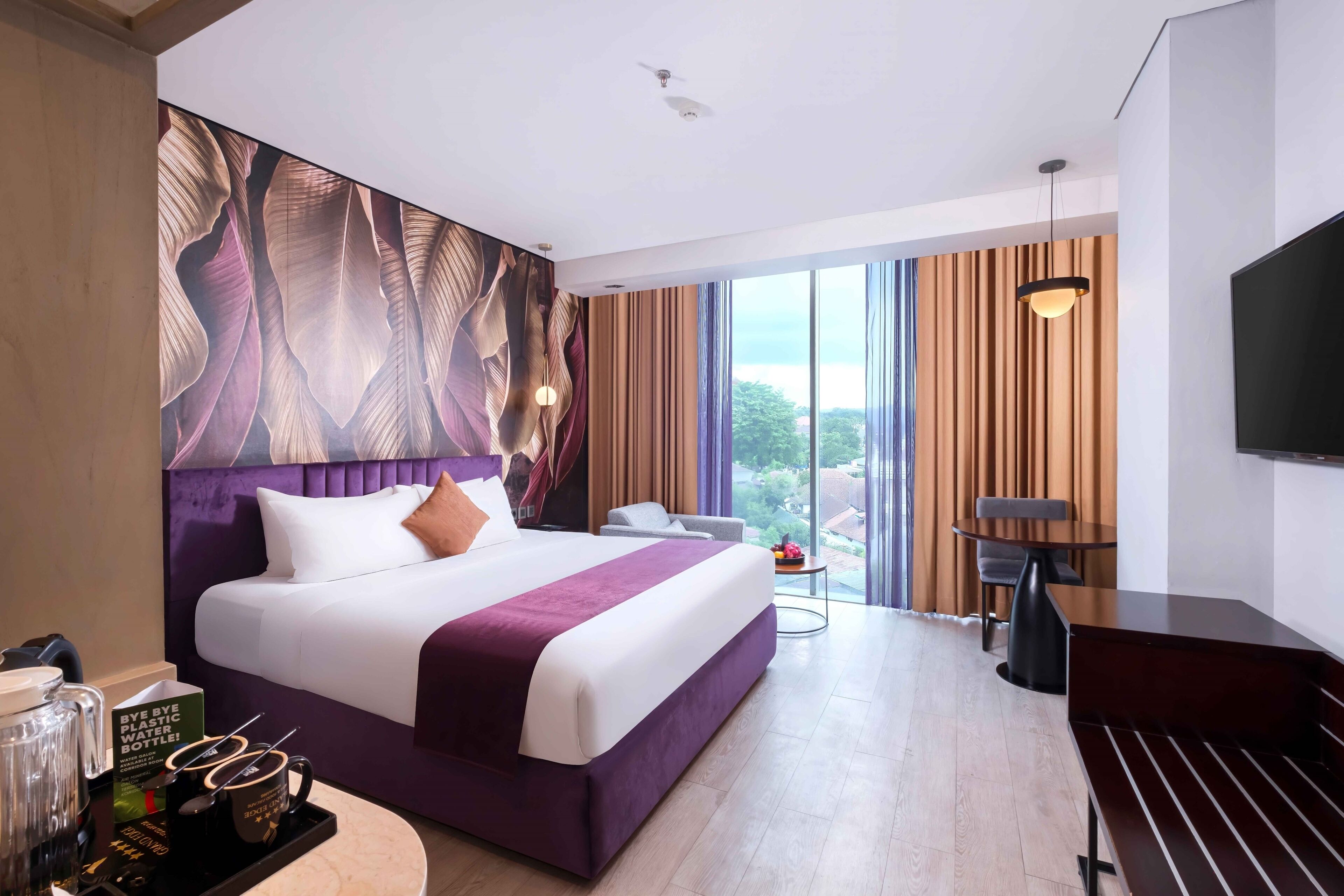 A modern hotel room with a large bed, a desk, a chair, a TV, and a view of the outdoors.