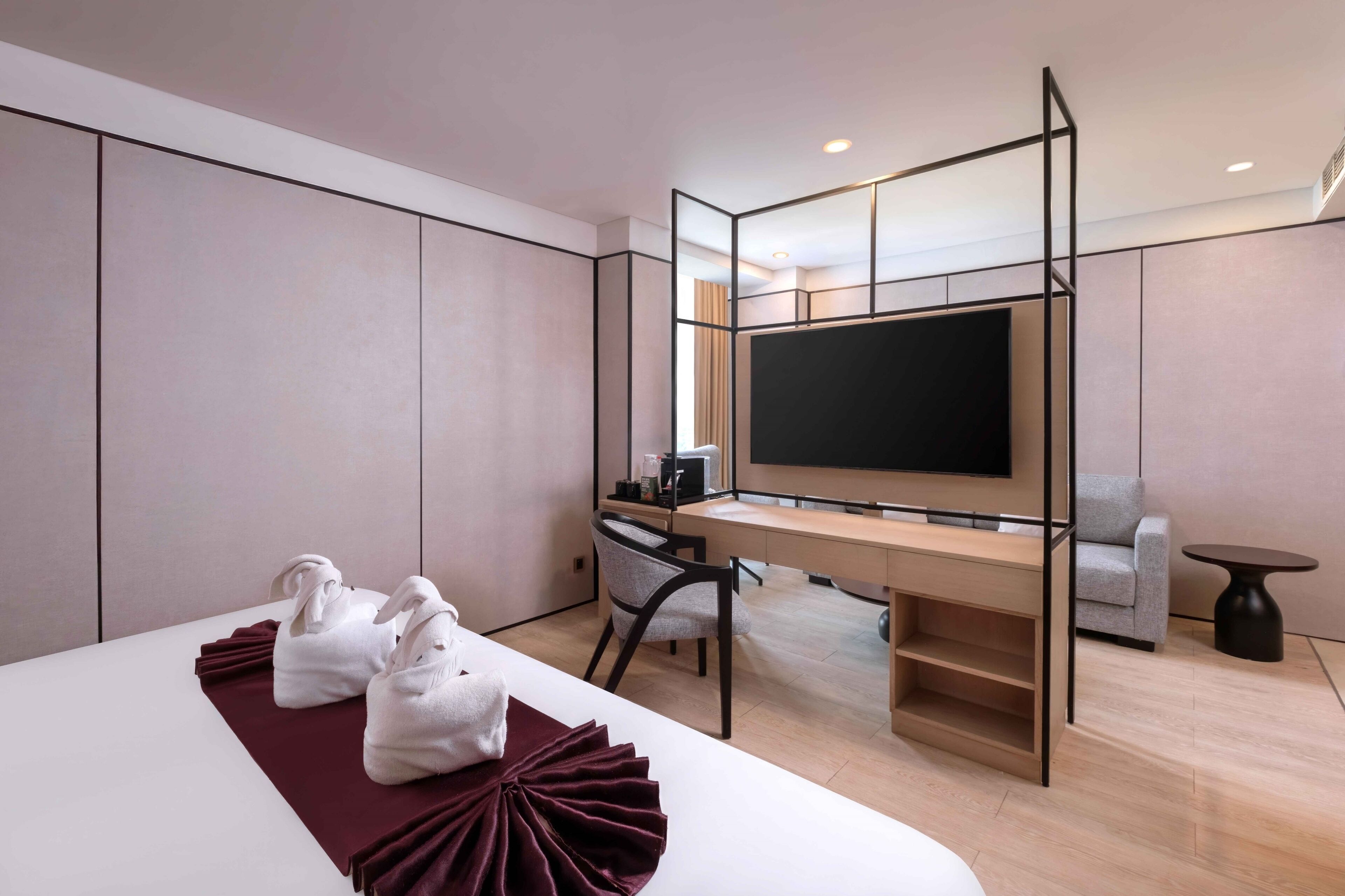 A modern hotel room with a bed, a desk with a computer, a TV, and a seating area.