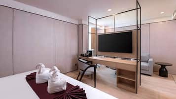 A modern hotel room with a bed, a desk with a computer, a TV, and a seating area.