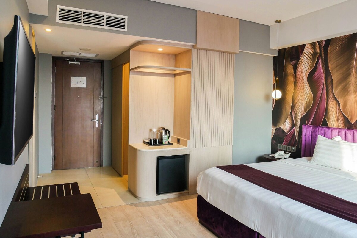 A hotel room with a bed, a desk, a mirror, and a wall with a leaf pattern.