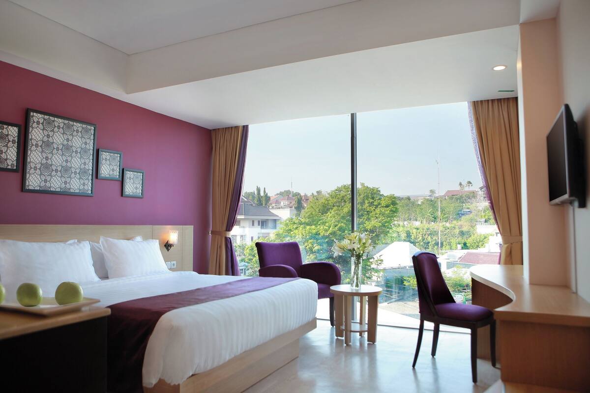 A hotel room with a large bed, a desk, two chairs, and a TV.