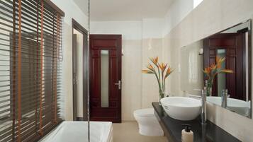 A modern bathroom with a bathtub, a white sink, a large mirror, and a door leading to another room.
