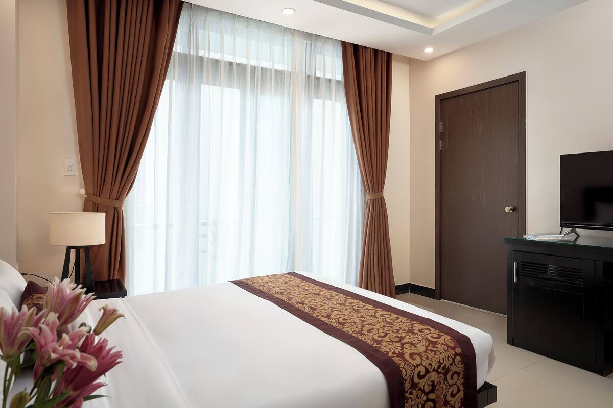A hotel room with a large bed, a TV, a desk, and a window with curtains.