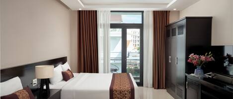 A hotel room with two beds, a TV, a desk, and a balcony with a view of buildings.