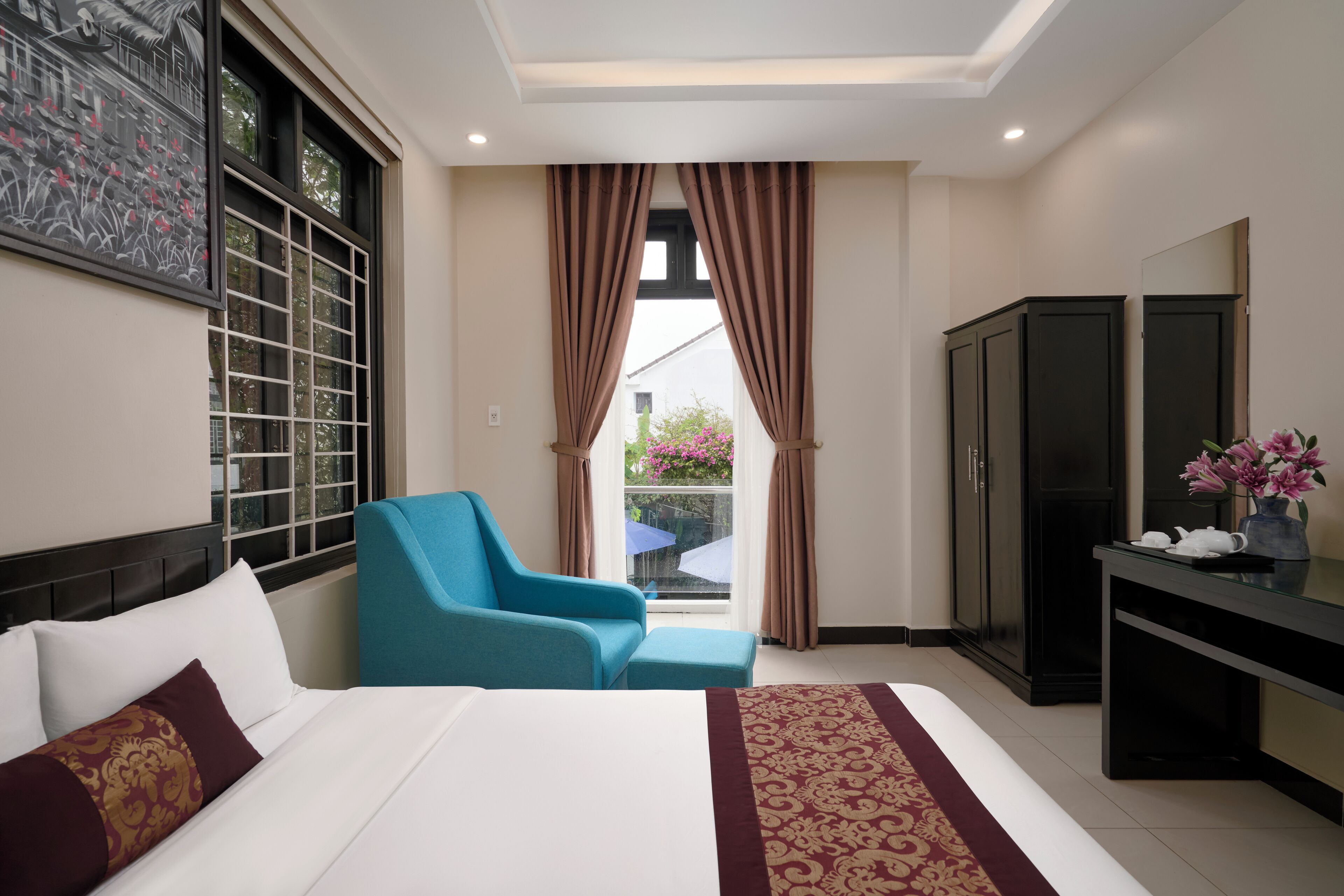 A hotel room with a bed, a blue armchair, a desk, and a wardrobe.