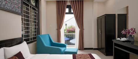 A hotel room with a bed, a blue armchair, a desk, and a wardrobe.