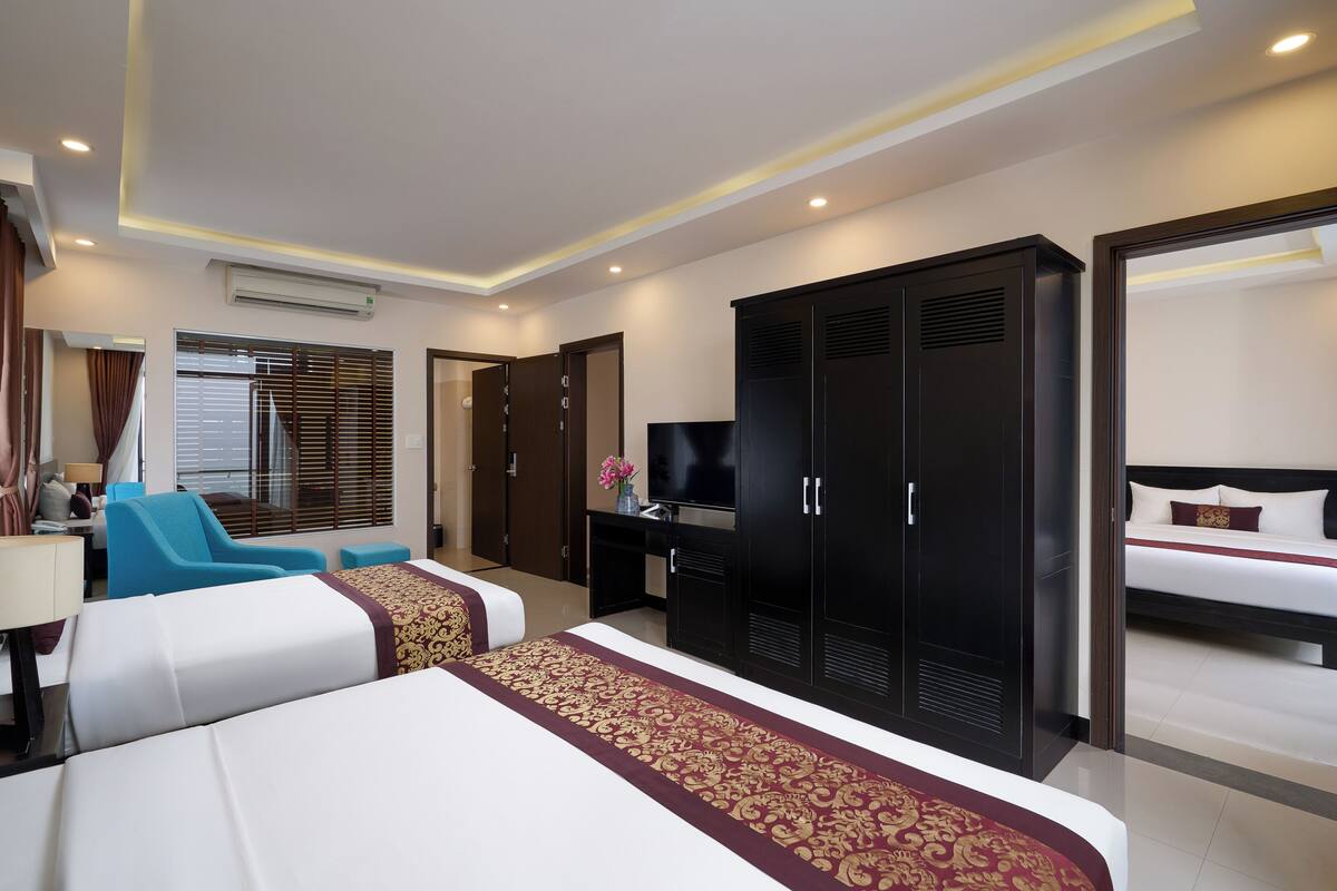 A hotel room with a large bed, a desk with a TV, a wardrobe, and a seating area with a chair and a sofa.