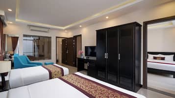 A hotel room with a large bed, a desk with a TV, a wardrobe, and a seating area with a chair and a sofa.