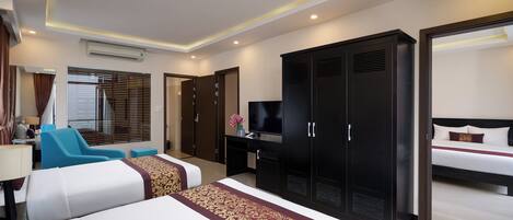 A hotel room with a large bed, a desk with a TV, a wardrobe, and a seating area with a chair and a sofa.