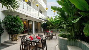 Un espace de restauration en plein air avec des tables pour deux, entouré d’une végétation luxuriante et illuminé par des lanternes jaunes suspendues.