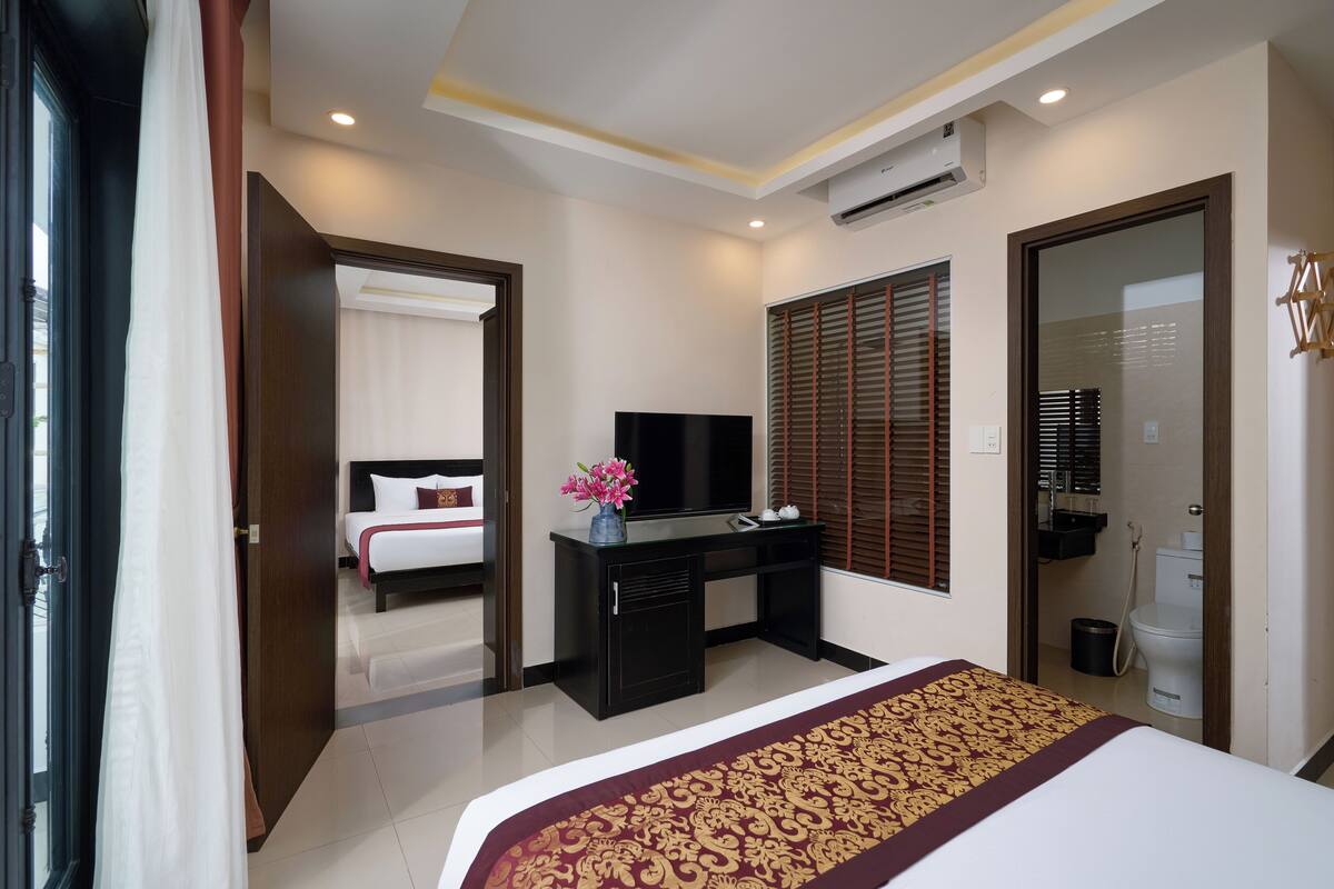 A hotel room with a bed, a desk with a TV, a bathroom, and a window with blinds.