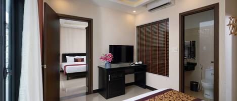 A hotel room with a bed, a desk with a TV, a bathroom, and a window with blinds.
