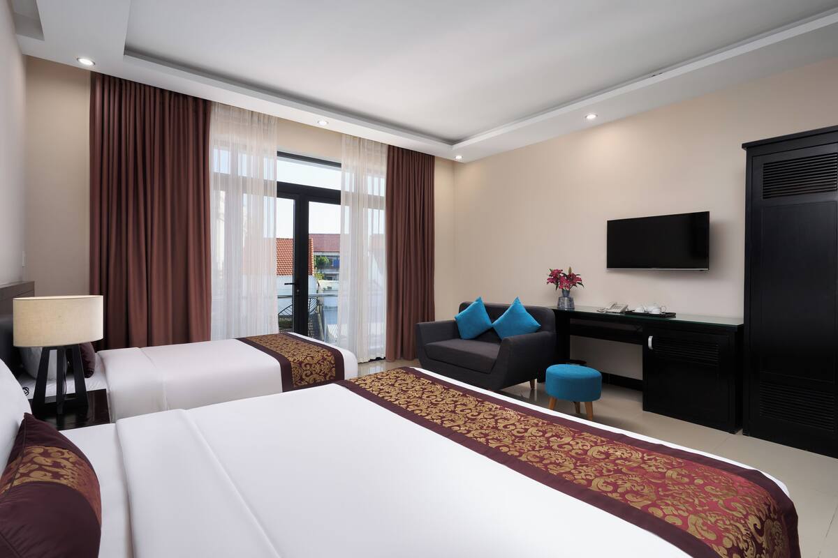 A hotel room with two beds, a desk, a TV, and a view of the outside.