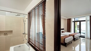 Une chambre d’hôtel avec une baignoire, une grande fenêtre avec des stores, un balcon avec une table et deux lits avec des oreillers.