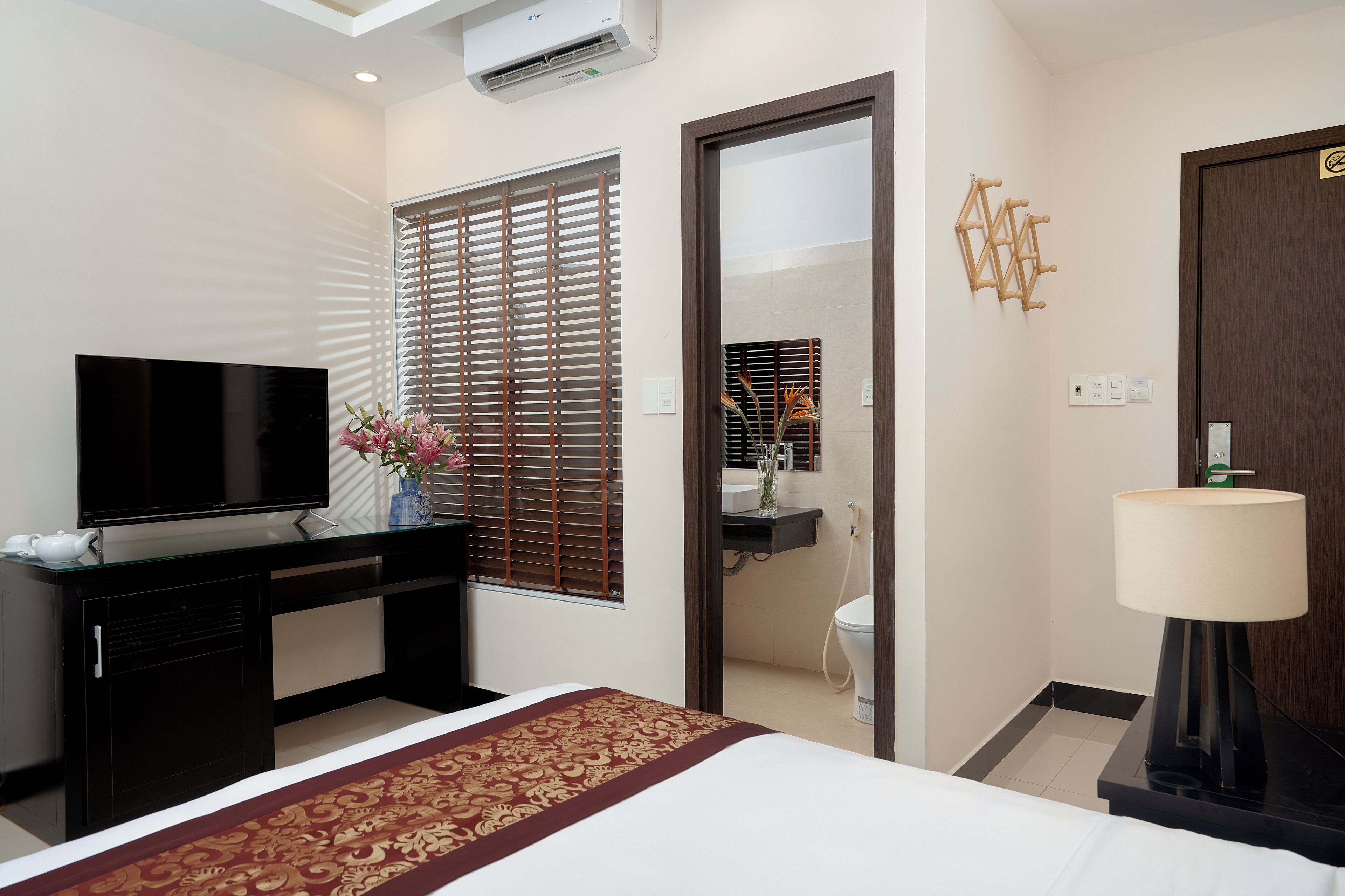 Une chambre d’hôtel avec un lit, un téléviseur posé sur un bureau, une salle de bain avec des toilettes et un miroir.