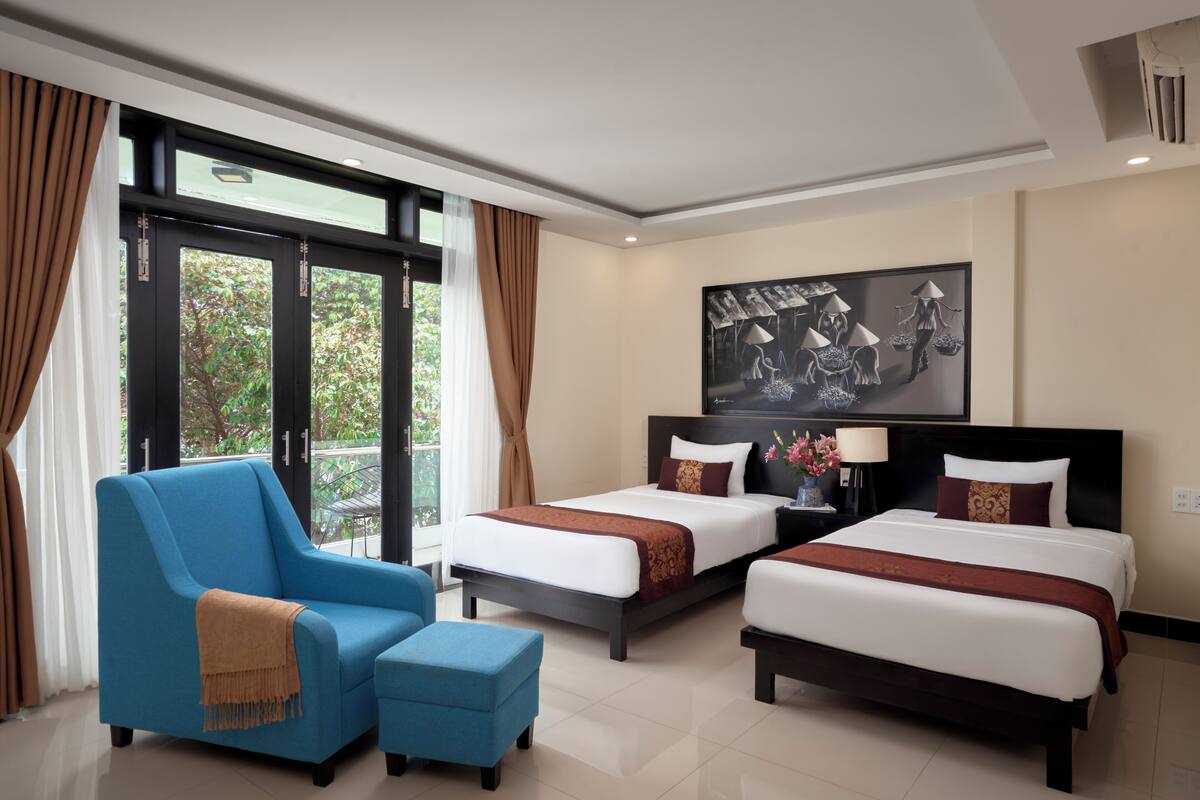 A hotel room with two beds, a blue armchair, and a small table.