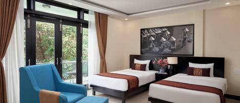 A hotel room with two beds, a blue armchair, and a small table.