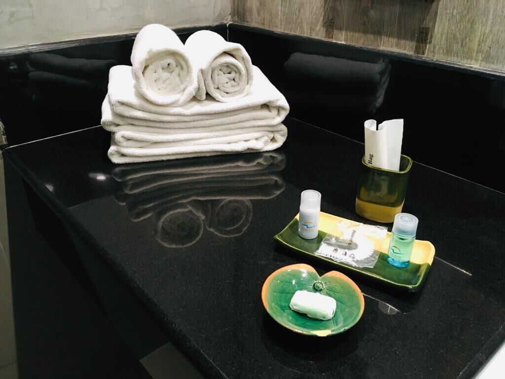 Una encimera negra con toallas blancas ordenadas, una bandeja verde con artículos de tocador y un cuenco verde con un objeto blanco.