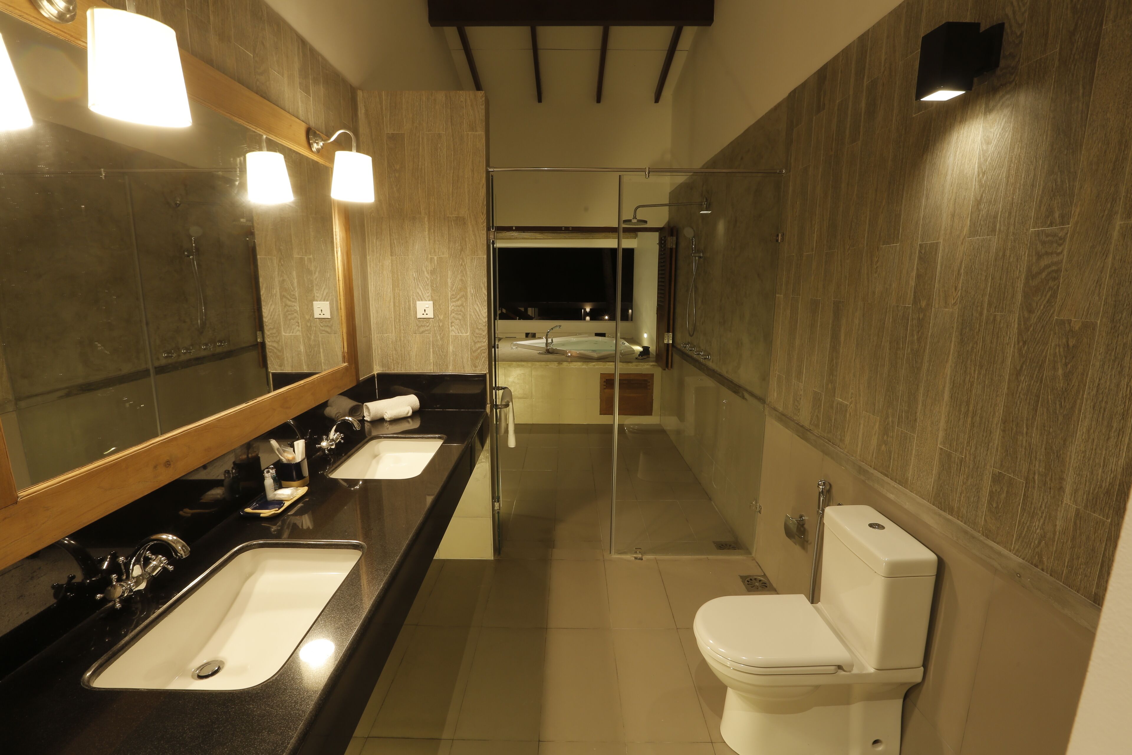 A modern bathroom with a large mirror, two sinks, a toilet, and a glass-enclosed shower area.